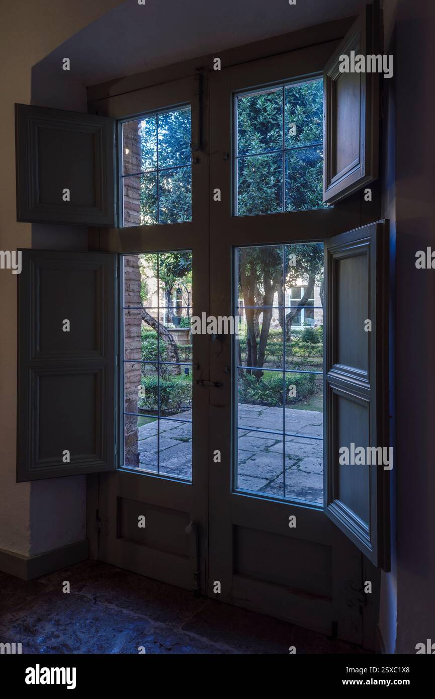 Vieille double porte en bois avec verre et panneaux menant au patio avec arbres et plantes dans le Parador de Turismo, ville d'Almagro, Ciudad Real, Espagne Banque D'Images