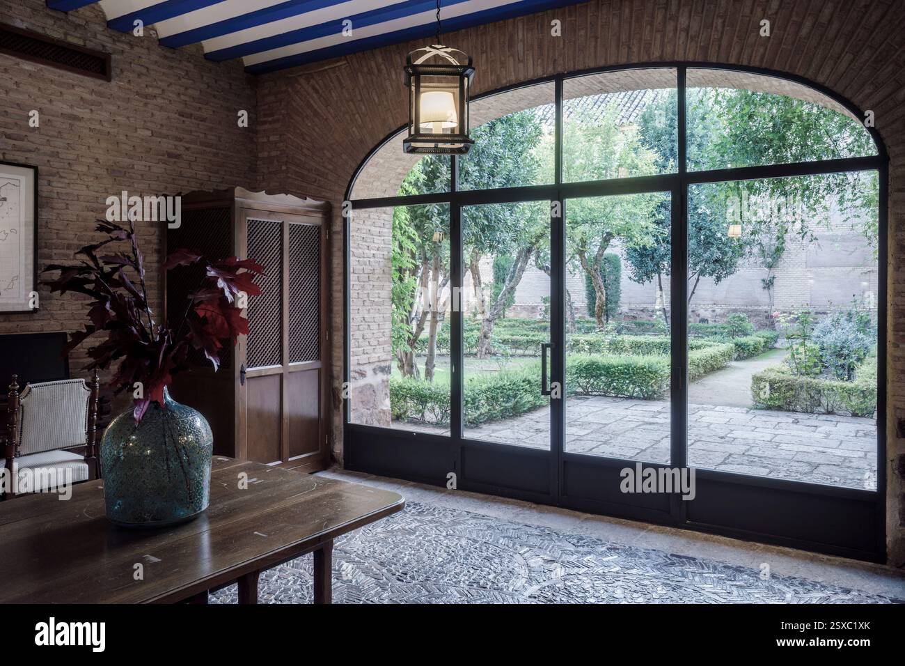 Vieille fenêtre en verre avec double porte en fer avec verre transparent menant au patio avec arbres et plantes dans le Parador de Turismo de Almagro, Espagne. Banque D'Images