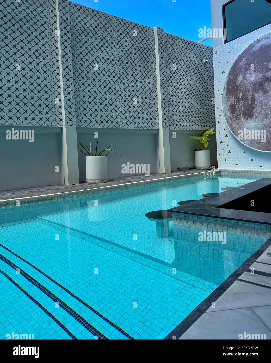 Piscine moderne avec mur décoratif et fresque lunaire Une piscine élégante avec un mur perforé gris clair et une fresque lunaire. L'eau cristalline reflète da - Image de stock capturée avec un smartphone