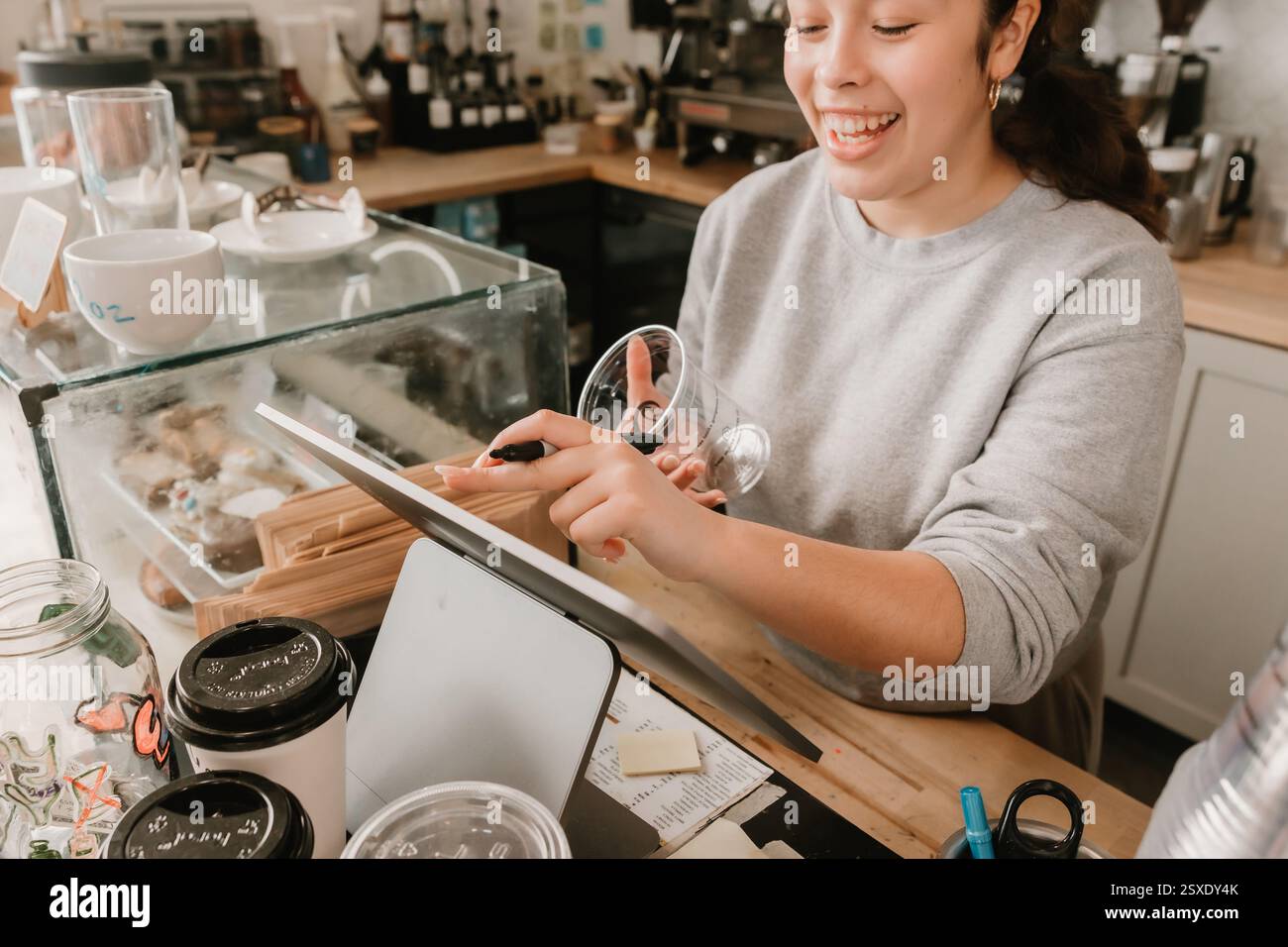 Barista souriant écrivant sur une tasse tout en prenant une commande au comptoir du café Banque D'Images