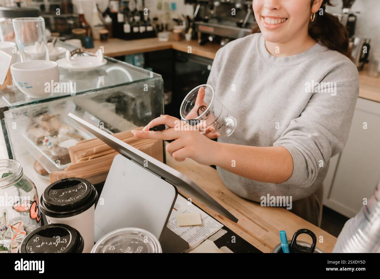 Barista souriant écrivant sur une tasse tout en prenant une commande au comptoir du café Banque D'Images