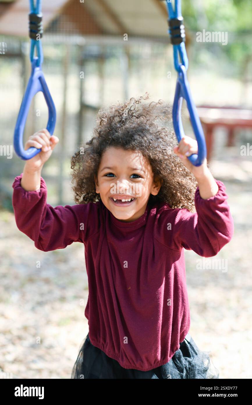 Enfant souriant accrochant des anneaux de terrain de jeu dans un décor extérieur lumineux Banque D'Images