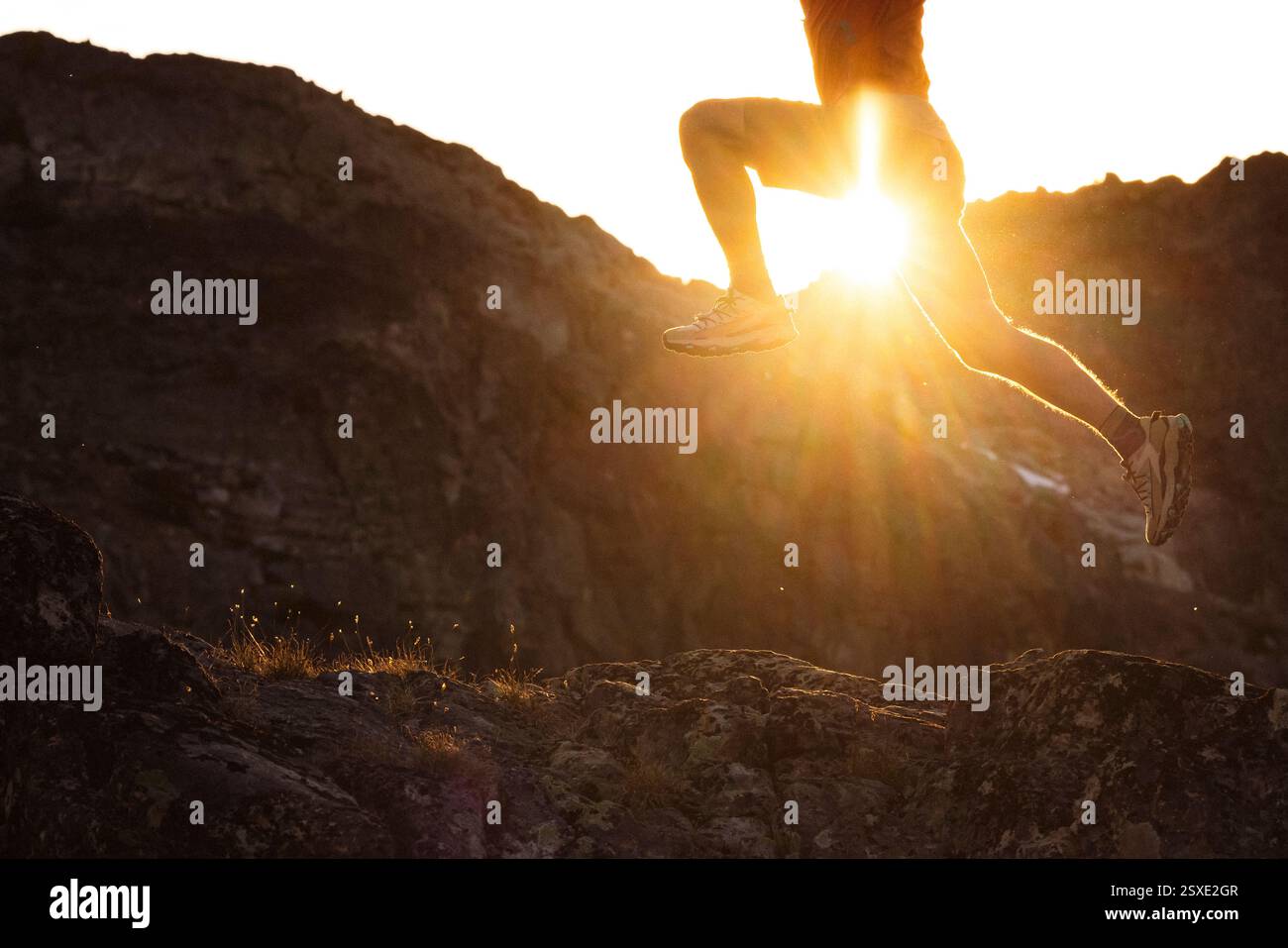 Un athlète de trail monte dans les airs avec le soleil derrière lui. Banque D'Images