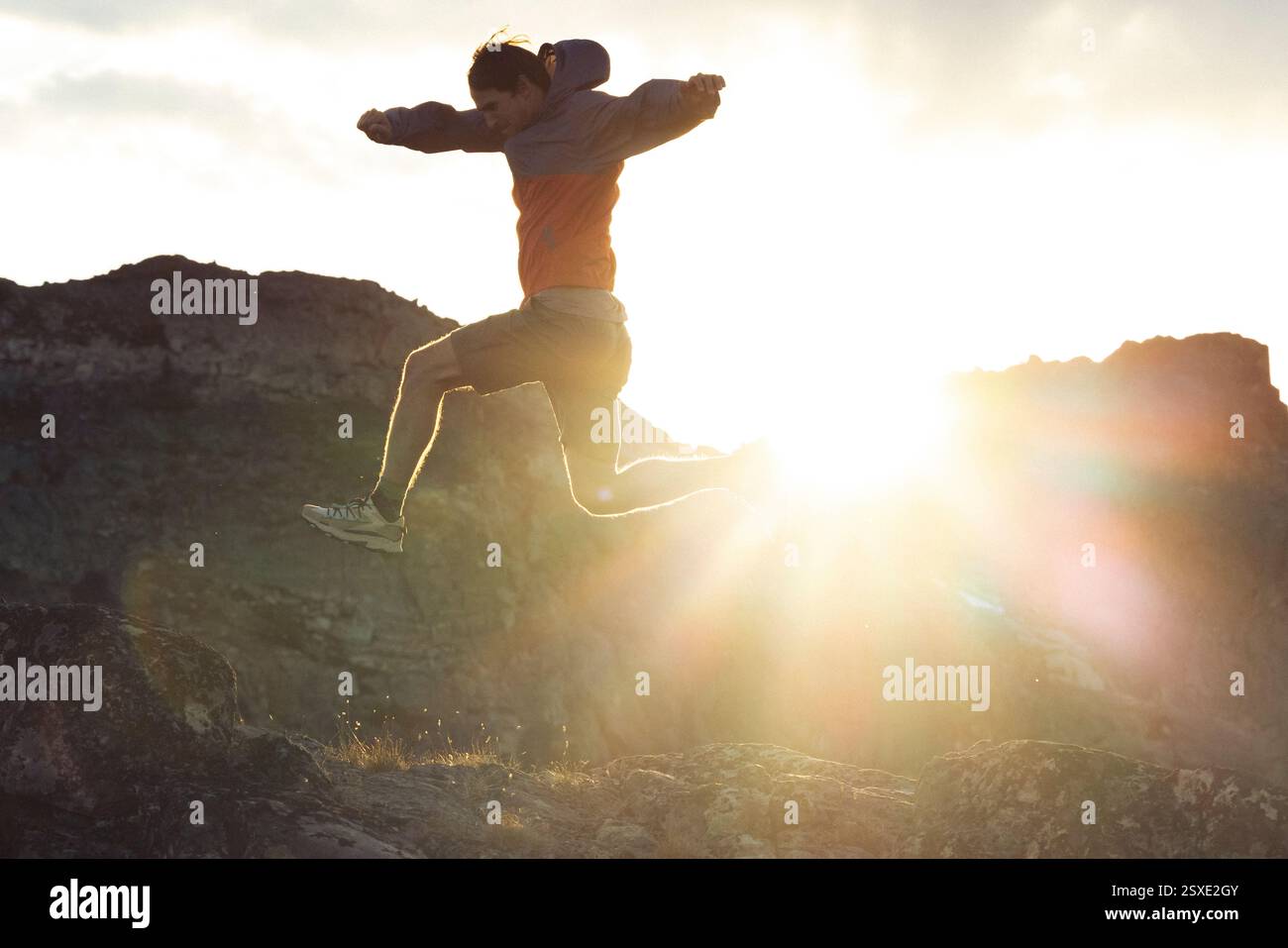 Un athlète de trail monte dans les airs avec le soleil derrière lui. Banque D'Images
