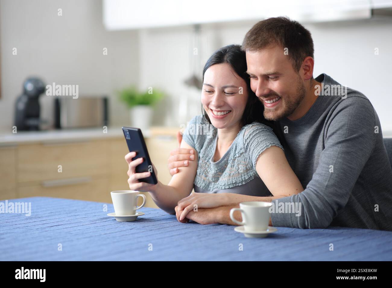 Heureux couple interracial dans l'amour vérifier le téléphone dans la cuisine à la maison Banque D'Images