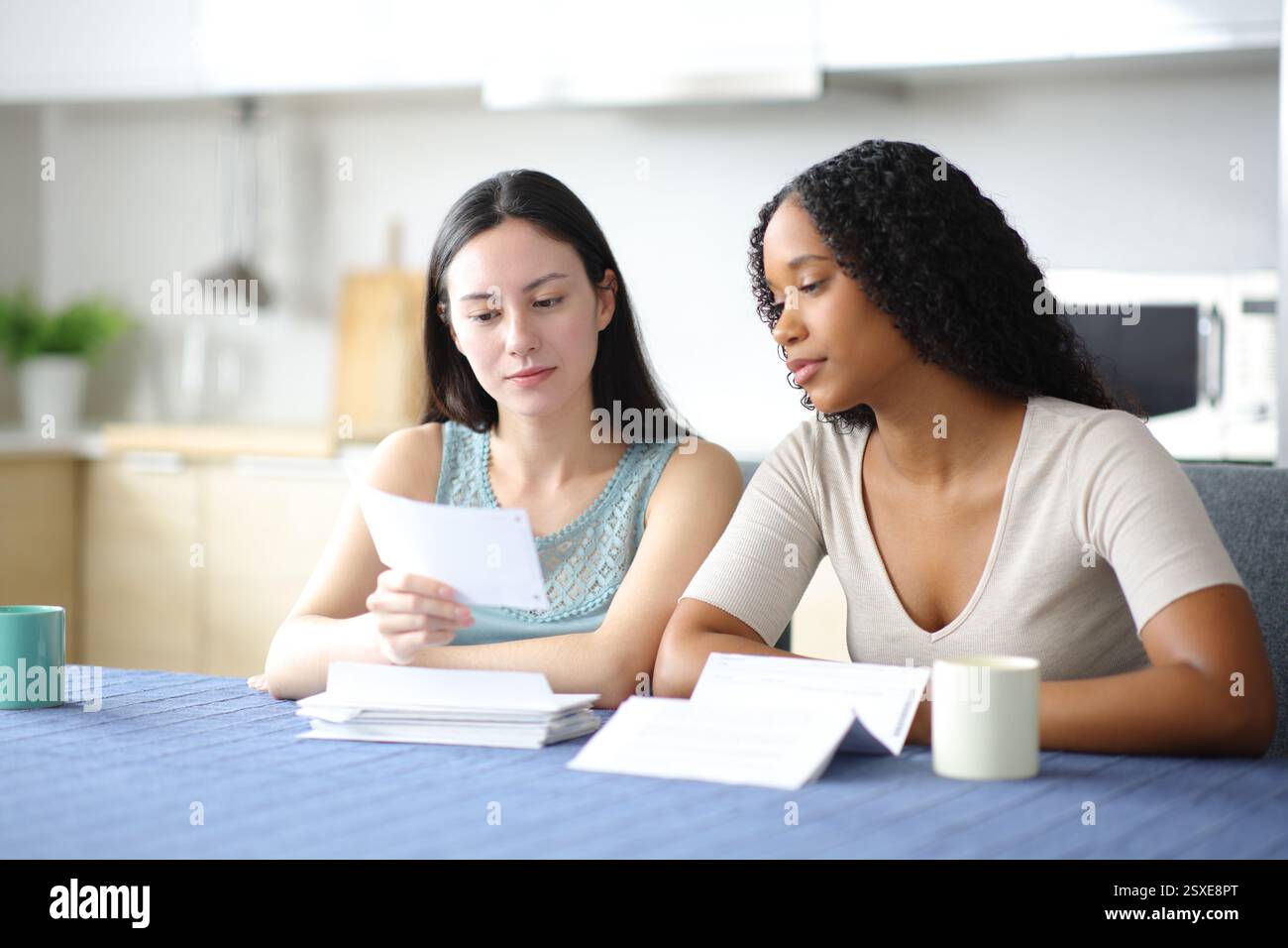 Femmes interraciales vérifiant les reçus dans la cuisine à la maison Banque D'Images