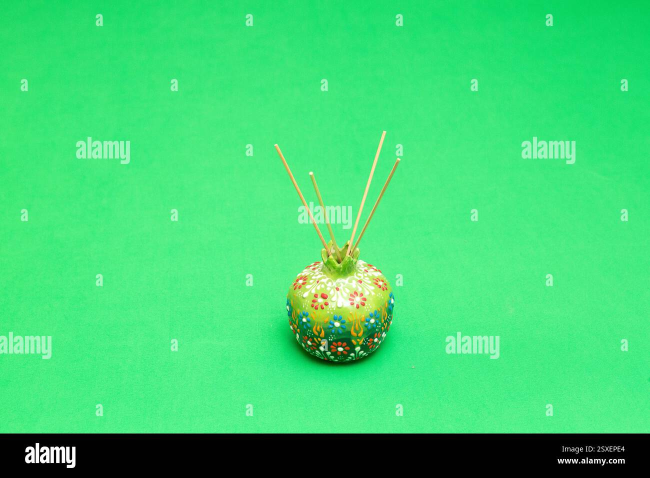 Porte-encens en forme de grenade en céramique verte libérant un parfum sur un fond vert vibrant, ajoutant une touche d'élégance et d'arôme Banque D'Images