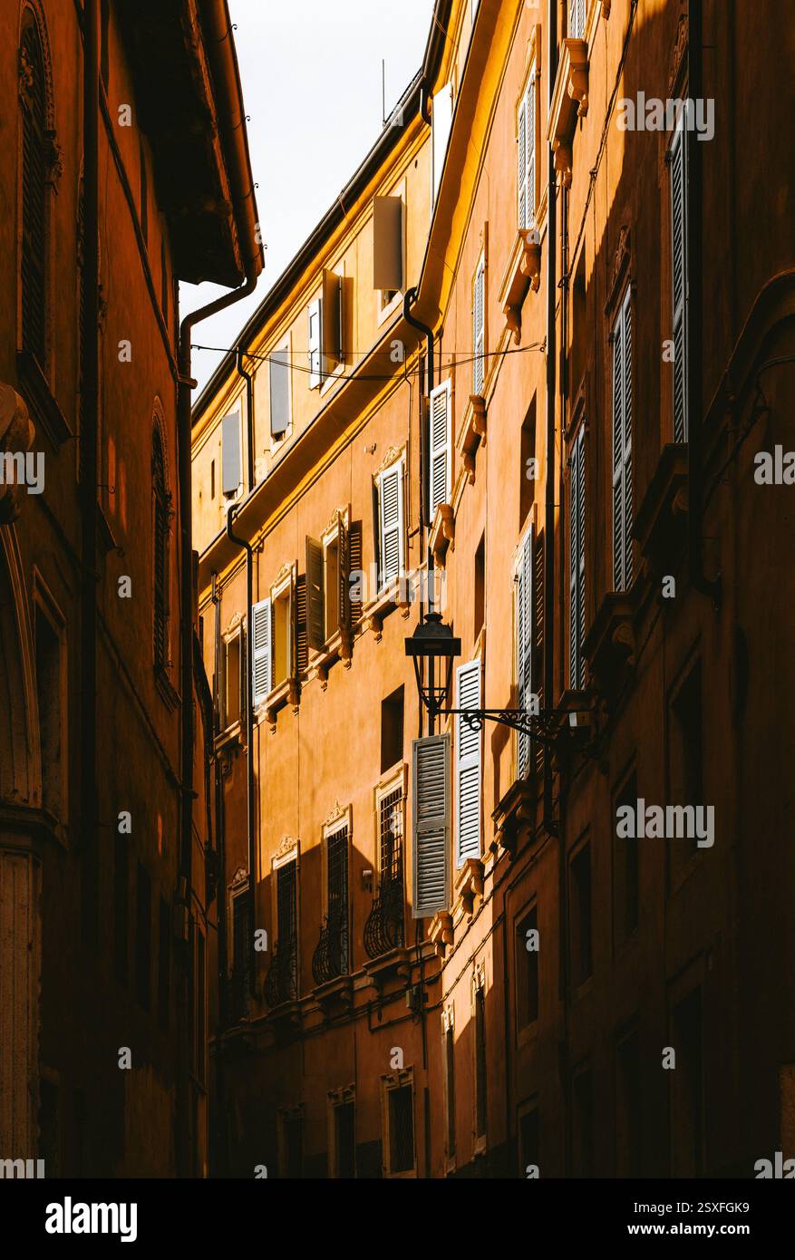 La lumière chaude du soleil illumine une rue étroite bordée de bâtiments traditionnels dotés de volets blancs et de balcons en fer forgé à Vérone, en Italie Banque D'Images
