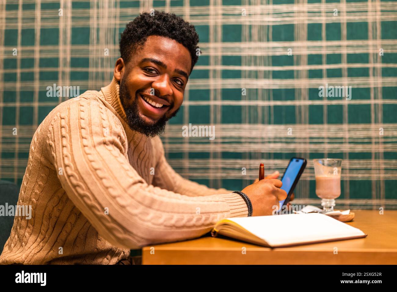 Freelance utilisant smartphone et bloc-notes. Il est assis dans le bar et fait des plans de travail. Banque D'Images