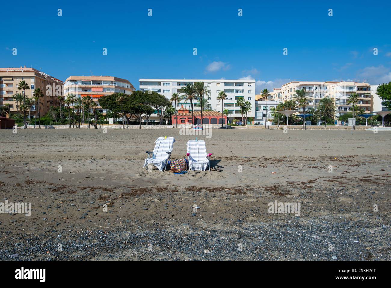 Deux chaises longues vides sur la plage et quelques hôtels et un ciel bleu en arrière-plan, photo d'Estepona Espagne. Banque D'Images