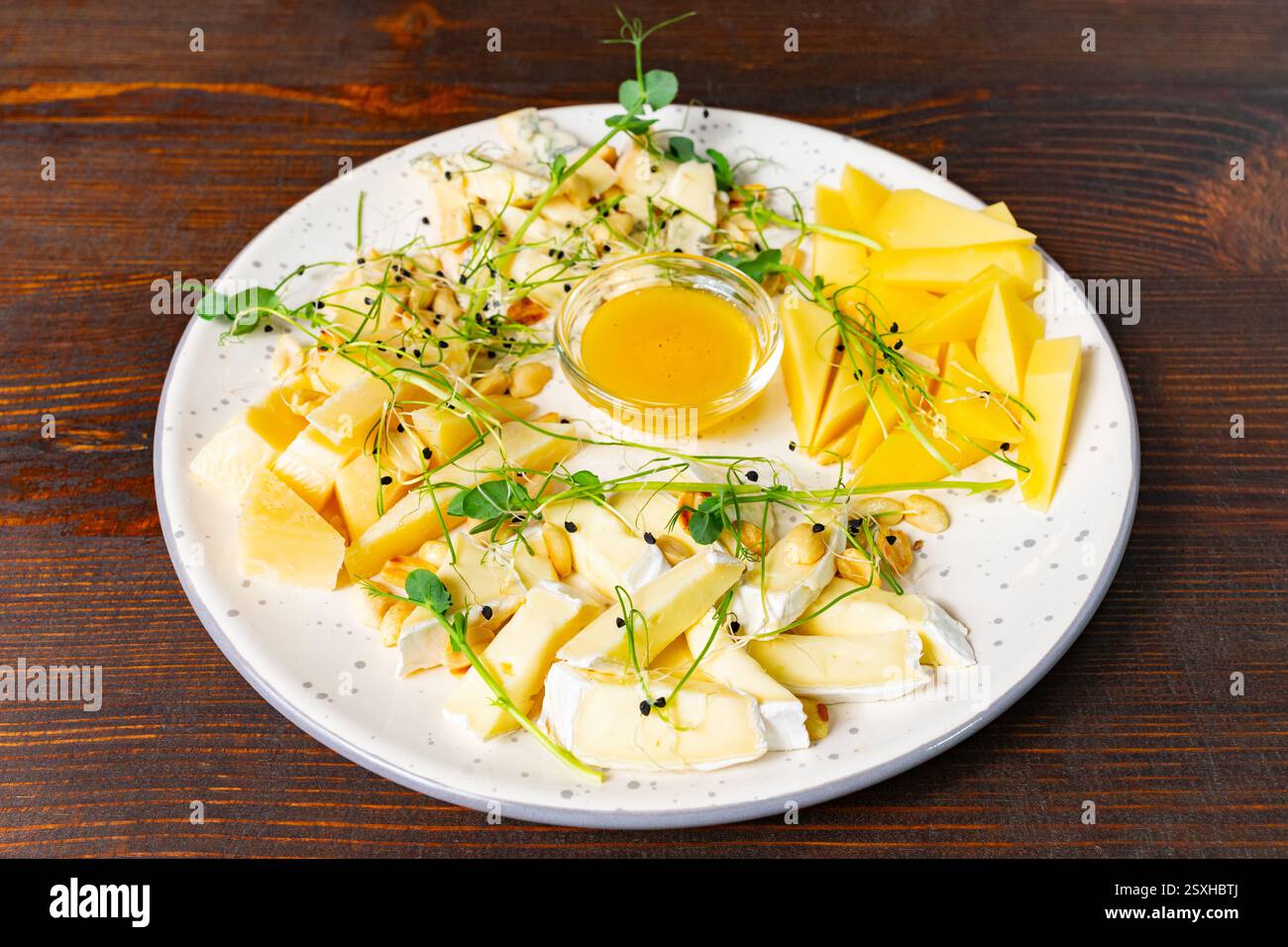 Un plateau de fromages magnifiquement arrangé présente une variété de fromages, une trempette au miel et des garnitures fraîches. La présentation met en évidence les textures et les couleurs o Banque D'Images