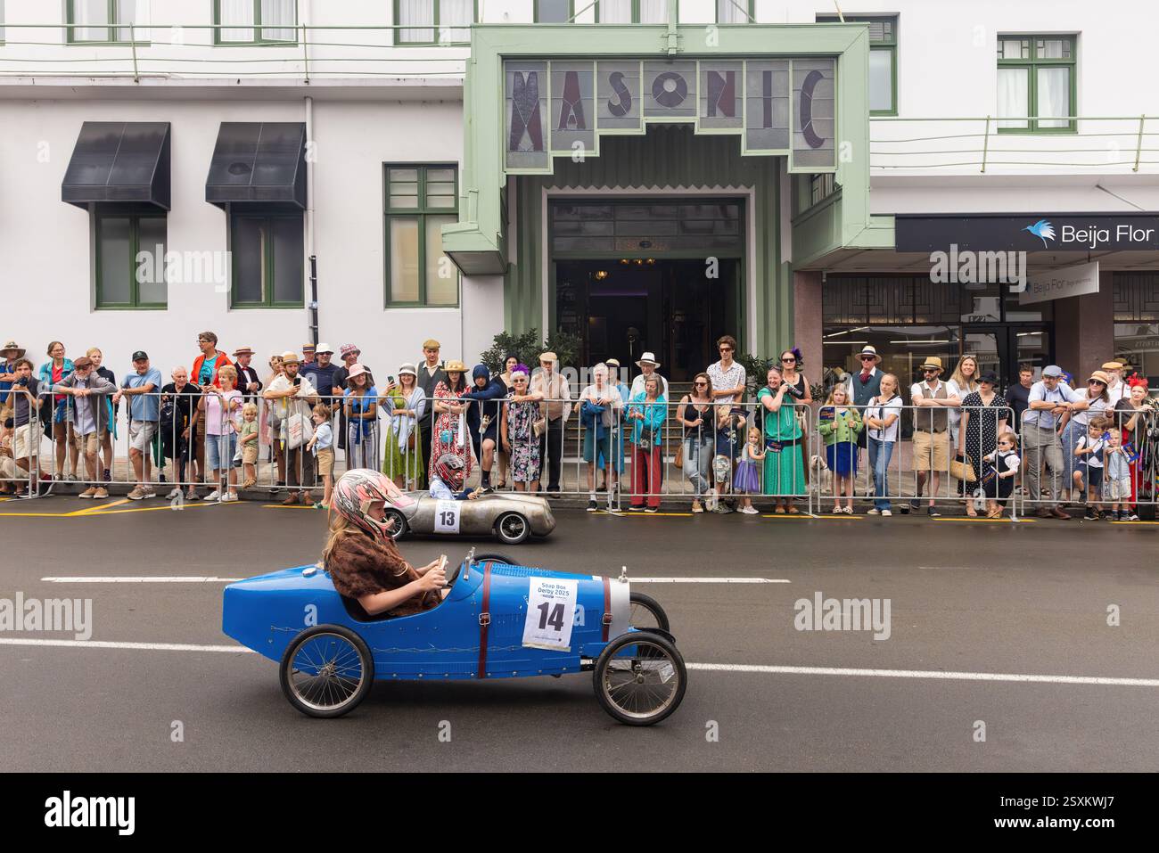 Course de derby Soapbox dans les rues de Napier, Nouvelle-Zélande, pendant le Festival Art Déco. Les enfants pédalent devant l'historique Hôtel maçonnique Banque D'Images