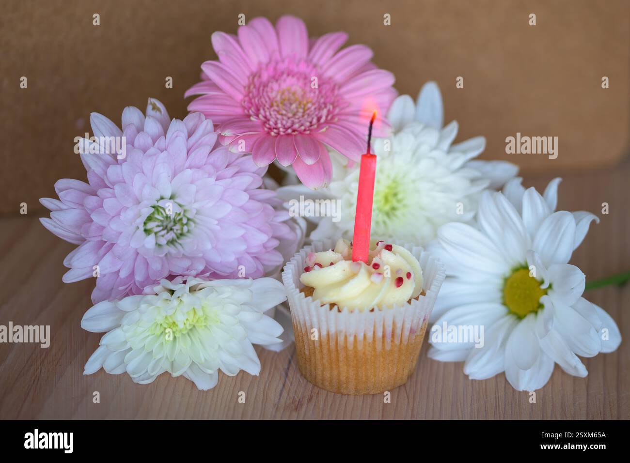 Cupcake coloré avec bougie entouré de fleurs vibrantes sur la surface en bois, ambiance chaleureuse, festive et festive. Banque D'Images