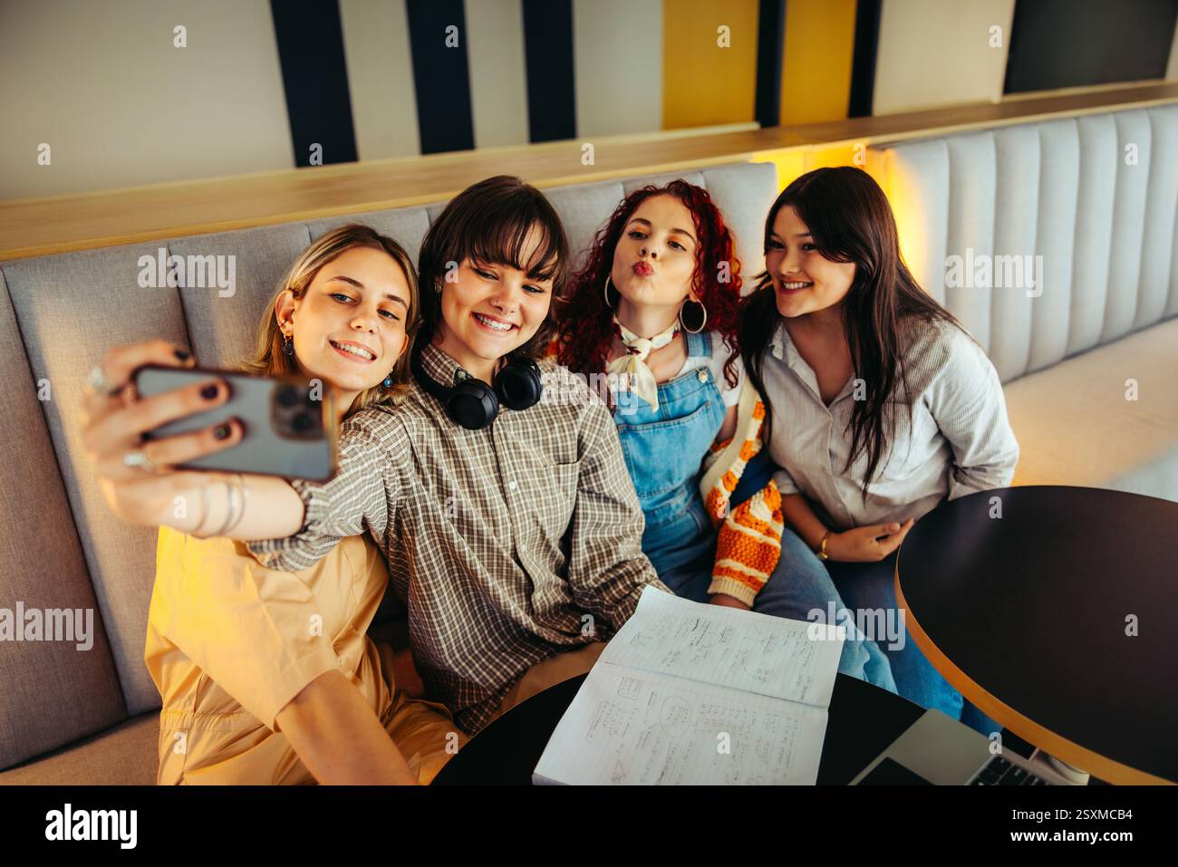 Quatre amis de la génération Z capturent un selfie joyeux dans un cadre de café moderne, mettant en valeur leur amitié étroite et leur sens de la mode diversifié. Banque D'Images