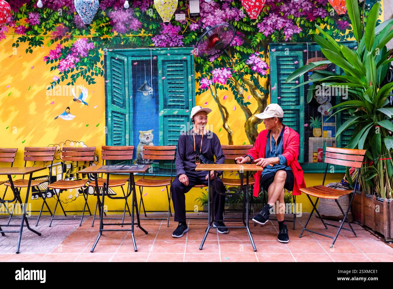 Deux hommes, portant des casquettes de baseball, assis dans un restaurant en plein air de train Street, le mur derrière eux est décoré de graffitis colorés. Banque D'Images