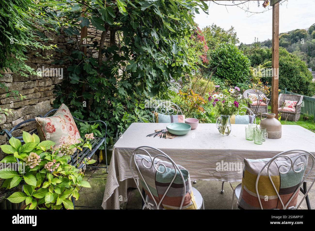Table et chaises ombragées par le figuier sur la terrasse du chalet Chalford tisserands dans les Cotswolds, Gloucestershire, Angleterre, Royaume-Uni. Banque D'Images