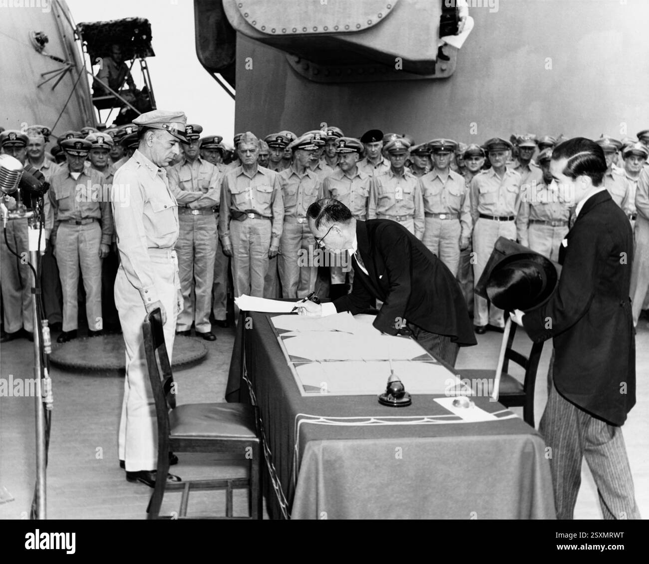 Le ministre japonais des Affaires étrangères Mamoru Shigemitsu signe l'instrument de reddition au nom du gouvernement japonais, à bord de l'USS Missouri (BB-63), le 2 septembre 1945. Le lieutenant-général Richard K. Sutherland, de l'armée américaine, regarde de l'autre côté de la table. Toshikazu Kase, représentant du ministère des Affaires étrangères, assiste Mr. Shigemitsu. Banque D'Images