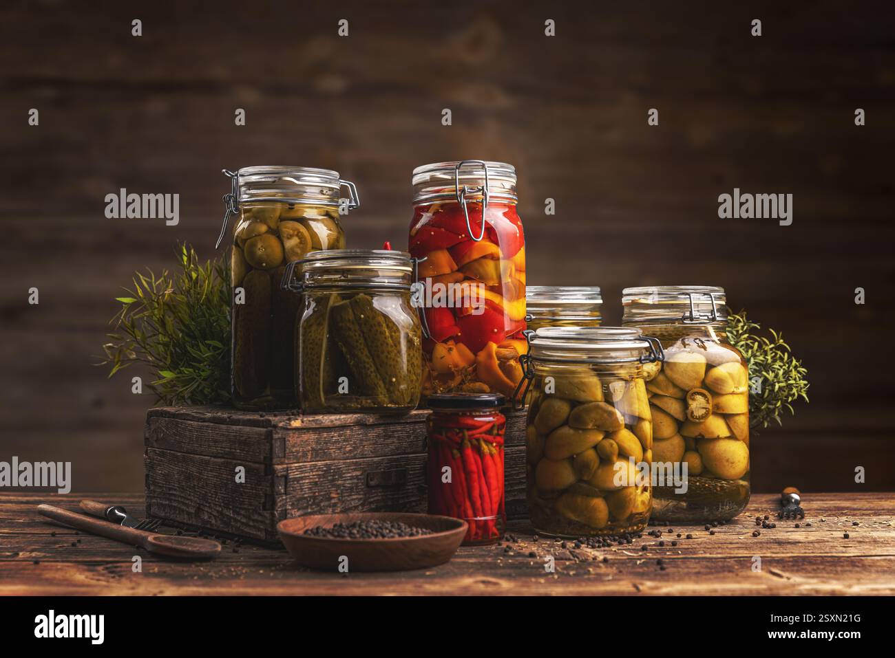 Des pots de légumes marinés comme les poivrons, les concombres et les tomates vertes sont disposés sur une table en bois rustique, mettant en valeur la technique de conservation maison Banque D'Images