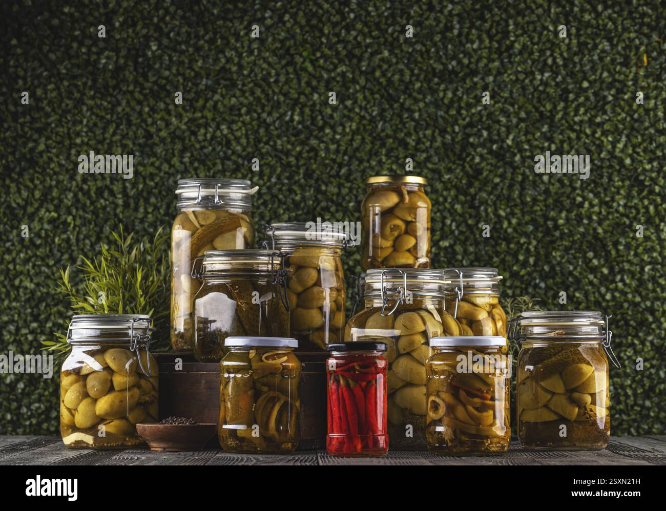 Des bocaux contenant des légumes marinés comme des concombres, des pommes de terre, des piments forts et des épices, créant un affichage coloré et appétissant sur un onglet en bois Banque D'Images