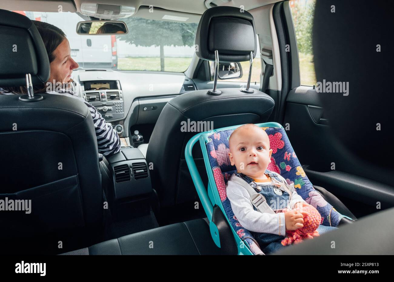 Portrait de bébé riant dans un siège d'auto tandis que mère conduisant une voiture de tourisme. Scène capture le moment de soin et de responsabilité, soulignant l'importance Banque D'Images