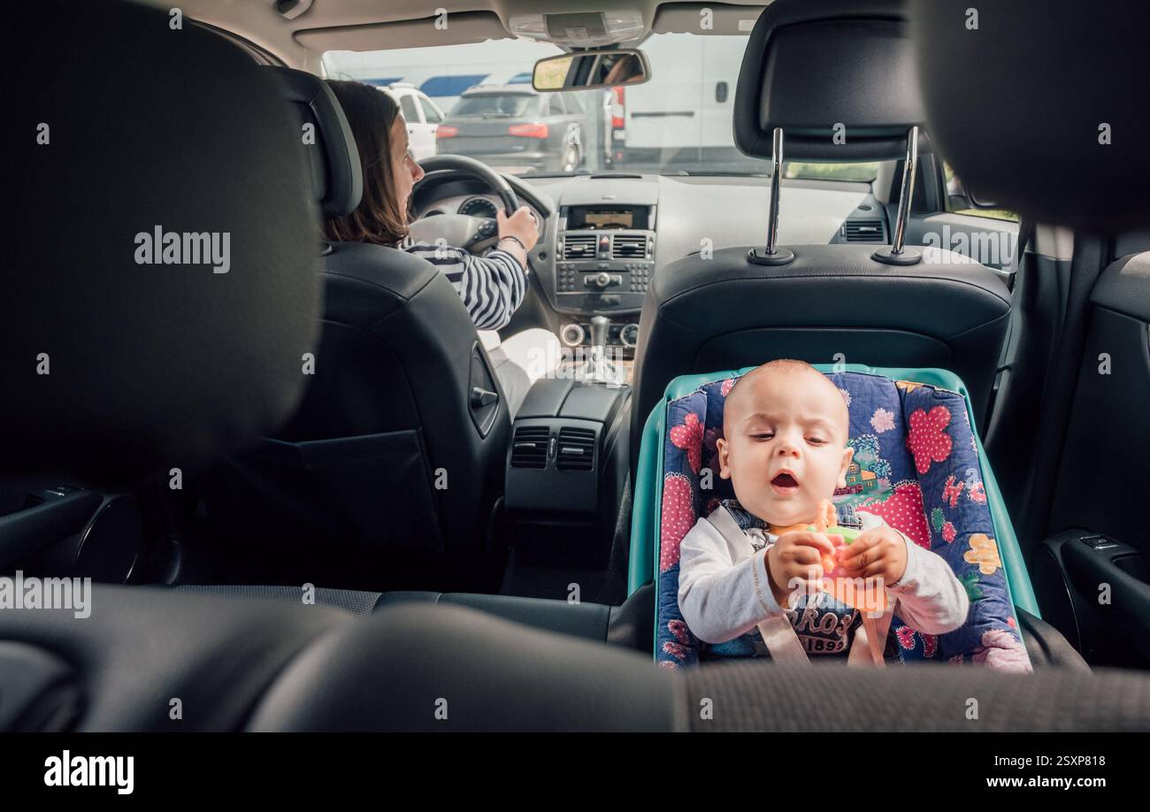 Portrait de bébé riant dans un siège d'auto tandis que mère conduisant une voiture de tourisme. Scène capture le moment de soin et de responsabilité, soulignant l'importance Banque D'Images