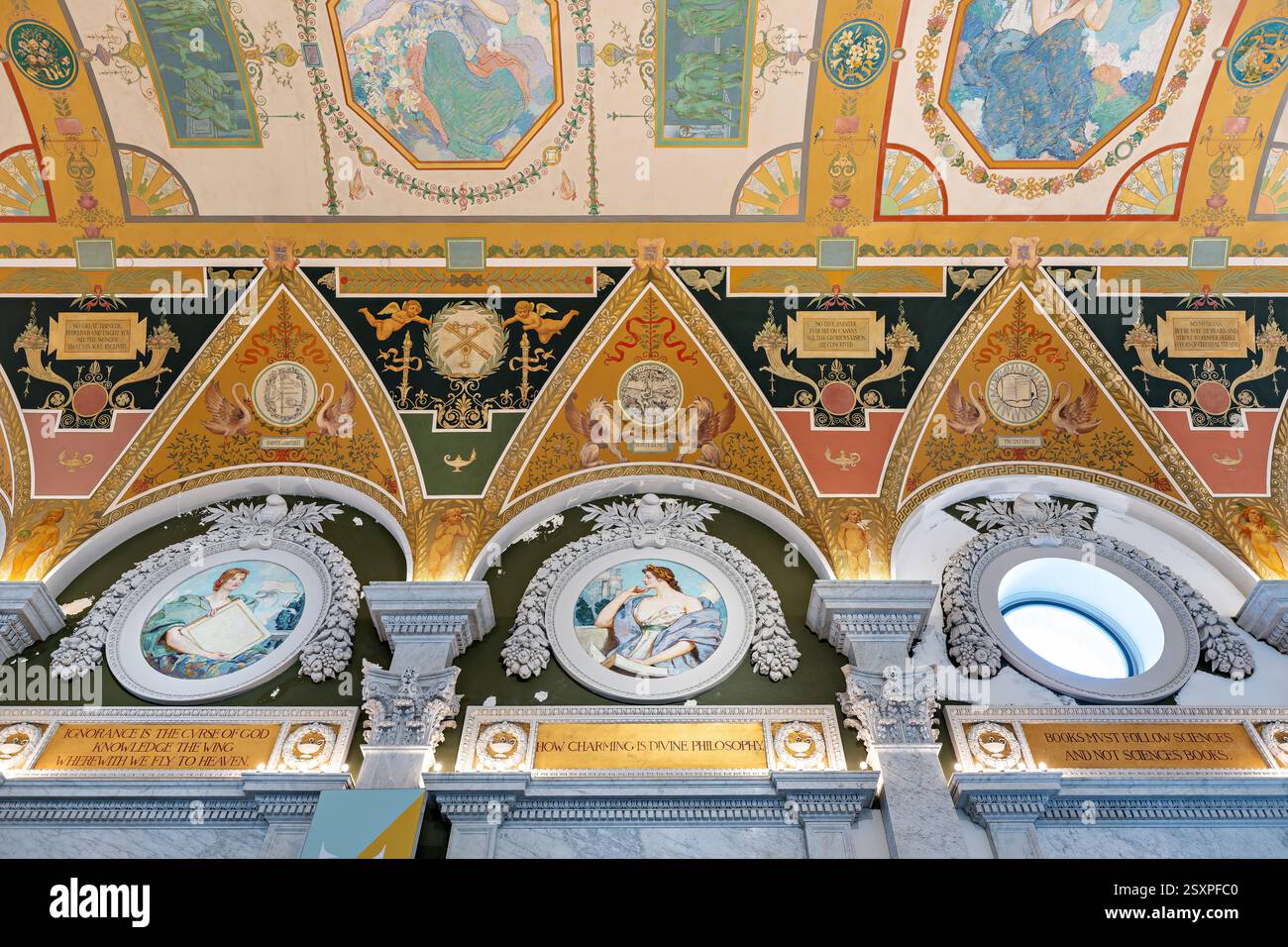 WASHINGTON DC — le plafond richement décoré du Grand Hall de la Bibliothèque du Congrès Thomas Jefferson Building présente des ornements métalliques élaborés découverts au cours des rénovations des années 1980 comme étant des feuilles d'aluminium plutôt que de l'argent. Achevé en 1897, le plafond présente six grands puits de lumière avec un motif à l'échelle qui reflète le sol en marbre sous-jacent. Les coins du plafond sont ornés de figures ailées de génie sculptées par Philip Martiny, des emblèmes flanquant qui affichent des symboles traditionnels de l'apprentissage. Banque D'Images