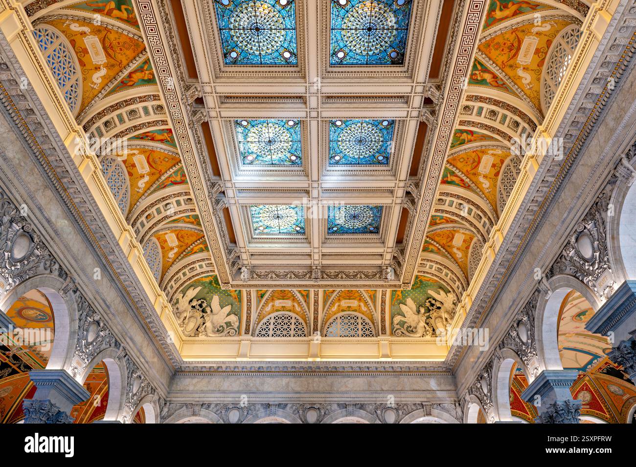 WASHINGTON DC — le plafond richement décoré du Grand Hall de la Bibliothèque du Congrès Thomas Jefferson Building présente des ornements métalliques élaborés découverts au cours des rénovations des années 1980 comme étant des feuilles d'aluminium plutôt que de l'argent. Achevé en 1897, le plafond présente six grands puits de lumière avec un motif à l'échelle qui reflète le sol en marbre sous-jacent. Les coins du plafond sont ornés de figures ailées de génie sculptées par Philip Martiny, des emblèmes flanquant qui affichent des symboles traditionnels de l'apprentissage. Banque D'Images