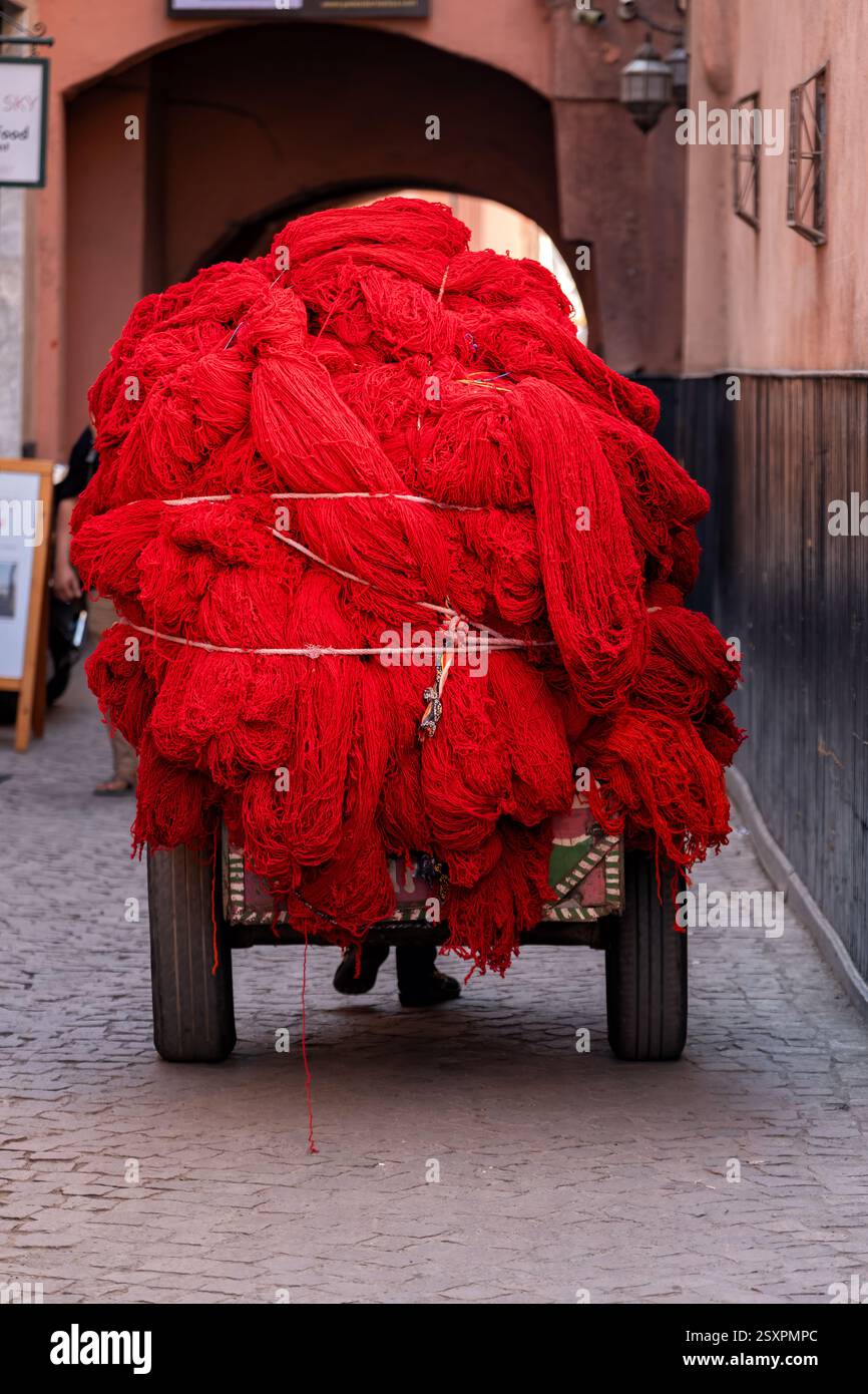 Marrakech Maroc. Un chariot à main lourdement chargé de laine teinte en rouge transporté à travers les souks centraux de la médina de Marrakech ou de la vieille ville Banque D'Images
