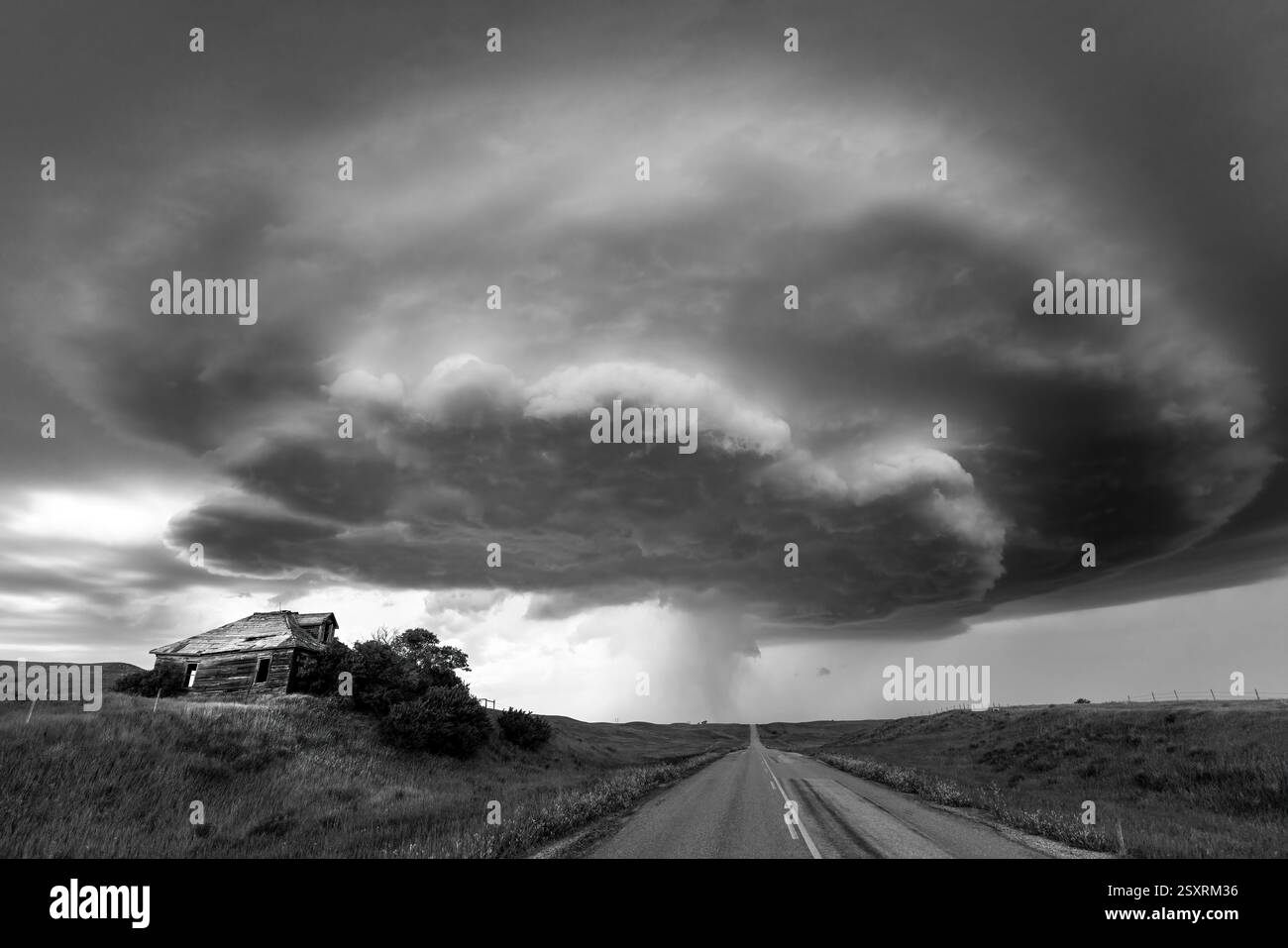 Paysage noir et blanc spectaculaire avec une tempête supercellulaire qui menace une ferme abandonnée et une route de campagne tranquille Banque D'Images
