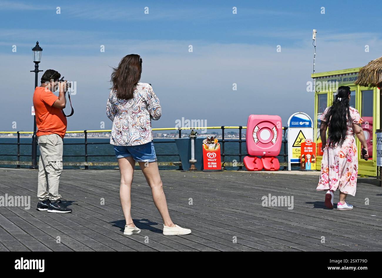 Un homme avec une chemise de thé orange prenant des photos à Pier Head par une journée ensoleillée à Southend on Sea. ROYAUME-UNI. Deux femmes en photo. Banque D'Images