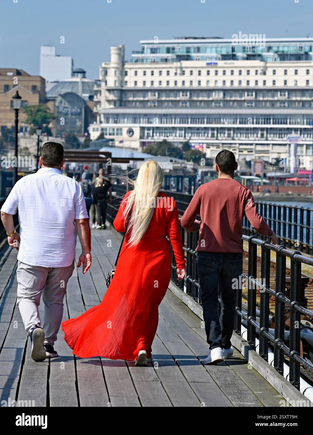 Une dame en rouge accompagnée de deux hommes marchant vers le rivage sur le plus long quai de plaisance du monde à Southend on Sea, ville de Southend. ROYAUME-UNI. Banque D'Images