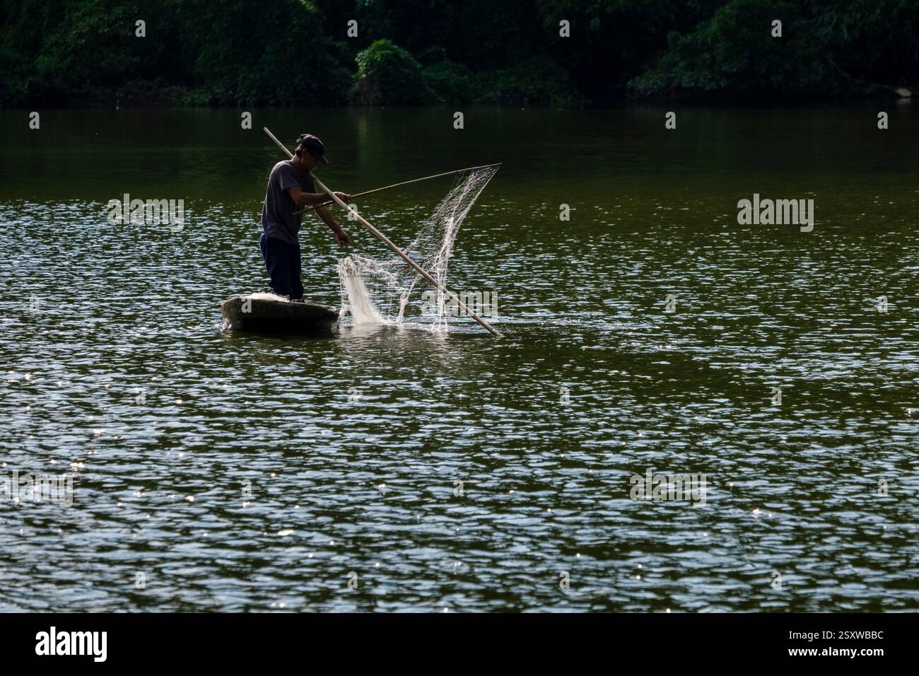 Un pêcheur pêche traditionnellement avec un filet d'un petit bateau sur une rivière. Banque D'Images