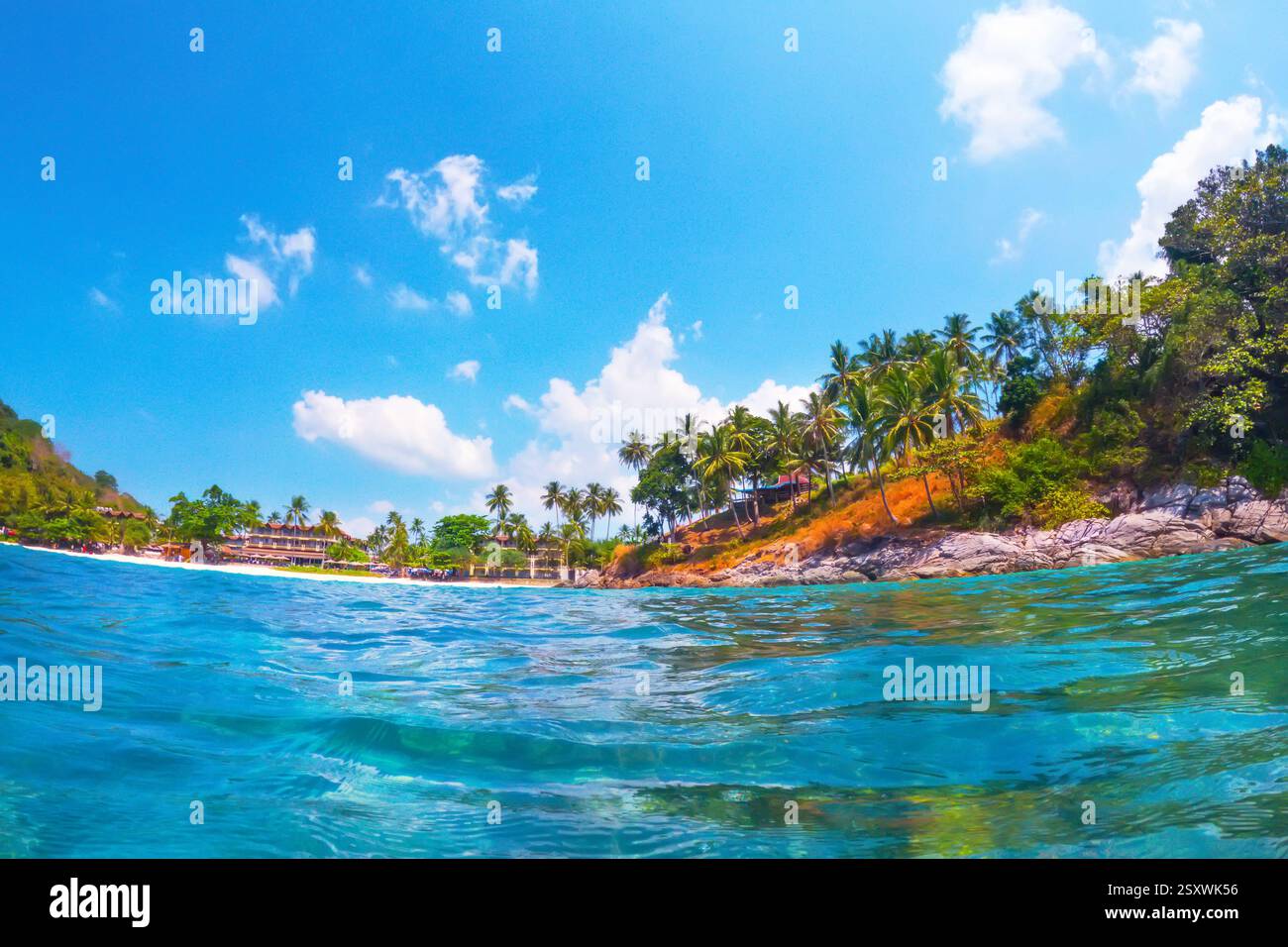 La lumière du soleil illumine les eaux turquoises vibrantes tandis que de douces vagues se jettent sur une plage de sable entourée de palmiers imposants et d'une végétation luxuriante Banque D'Images