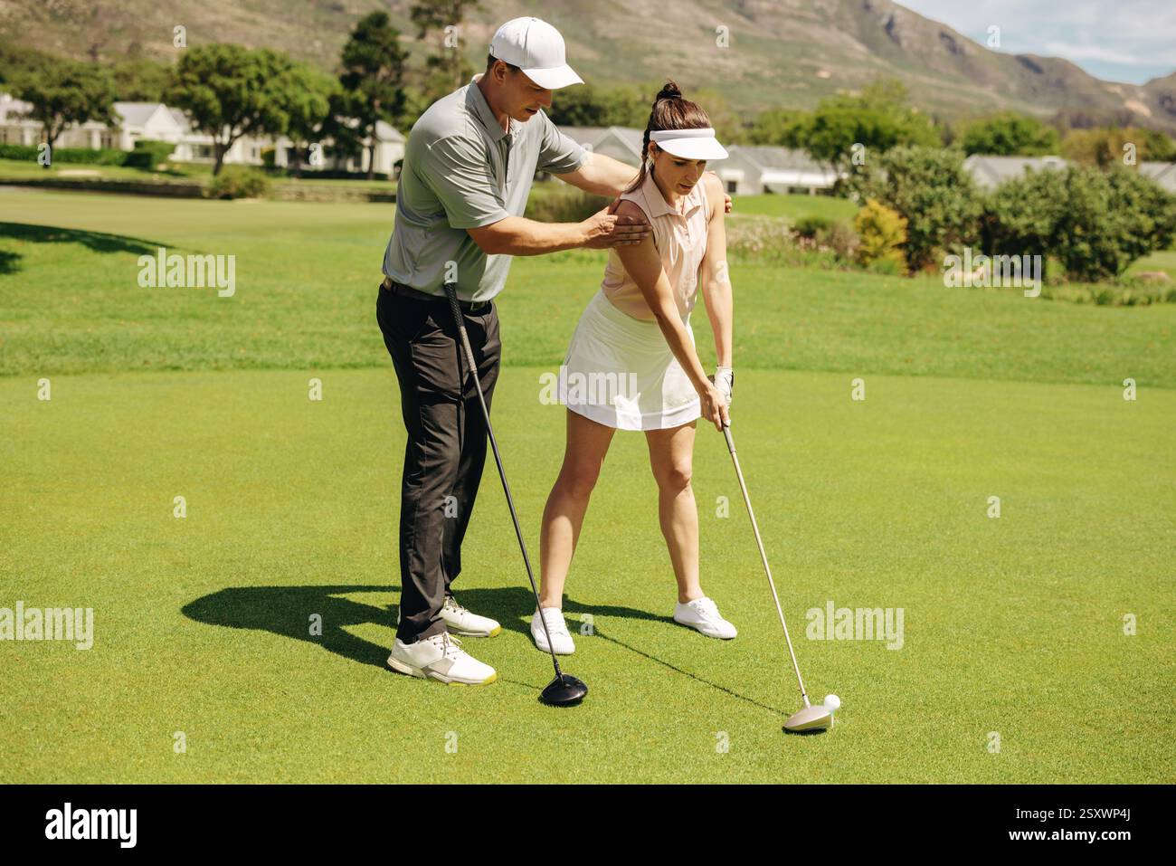 Un instructeur de golf guide une jeune femme sur sa position de put sur un green, mettant l'accent sur le développement des compétences et la confiance dans un complexe de golf serein Banque D'Images