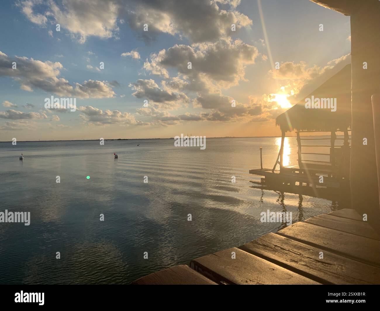 Coucher de soleil à couper le souffle sur des eaux calmes avec une jetée en bois rustique et une cabane au toit de chaume, créant une escapade tropicale sereine Banque D'Images