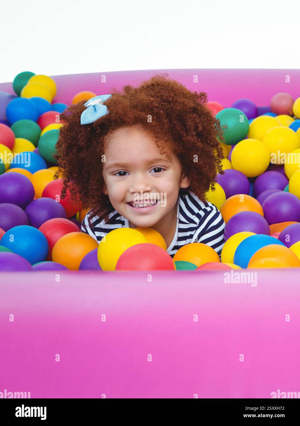 Enfant souriant jouant dans la fosse colorée de balle, profitant de l'activité d'intérieur amusante Banque D'Images