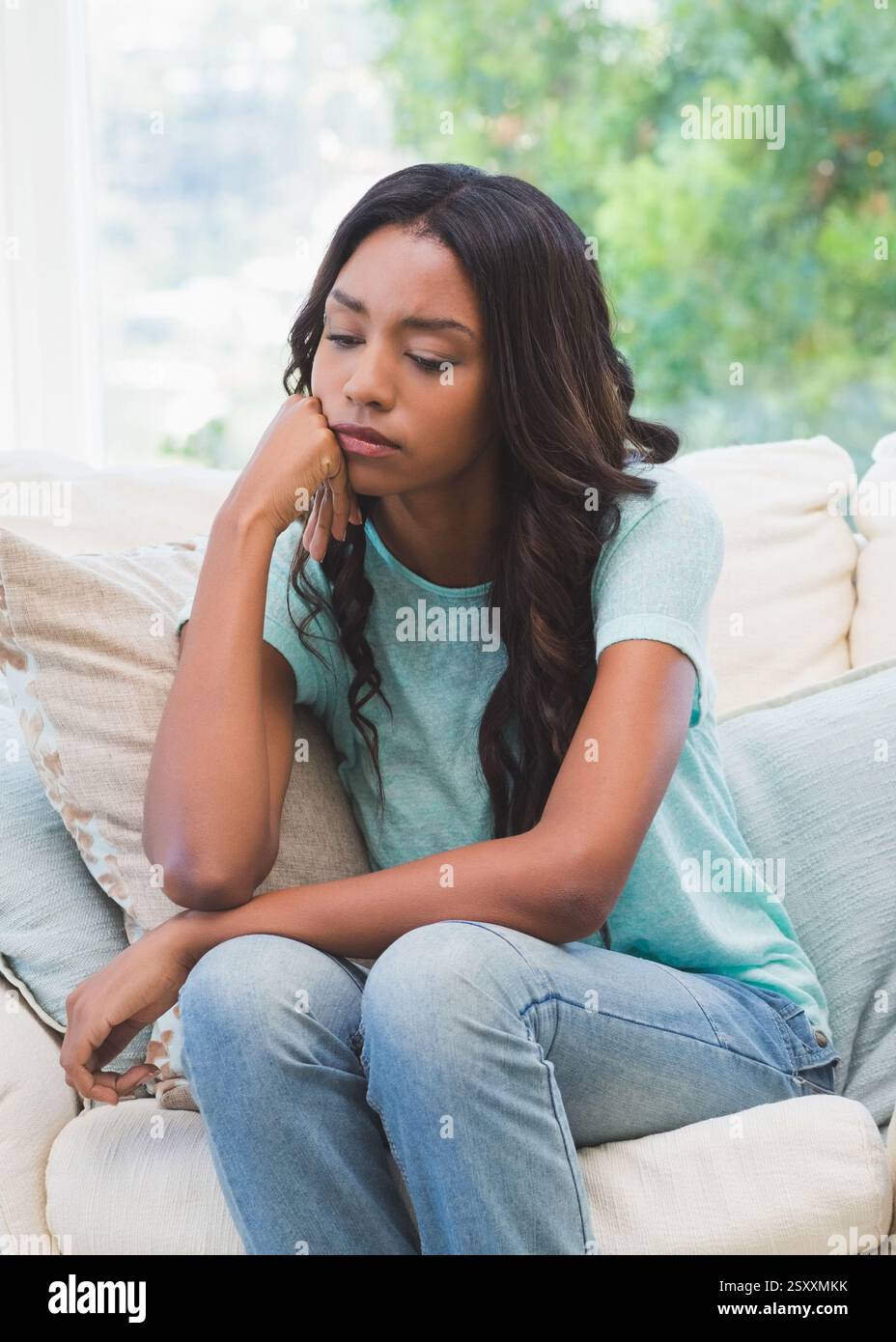 Femme réfléchie assise sur le canapé à la maison, regardant pensive et détendue Banque D'Images