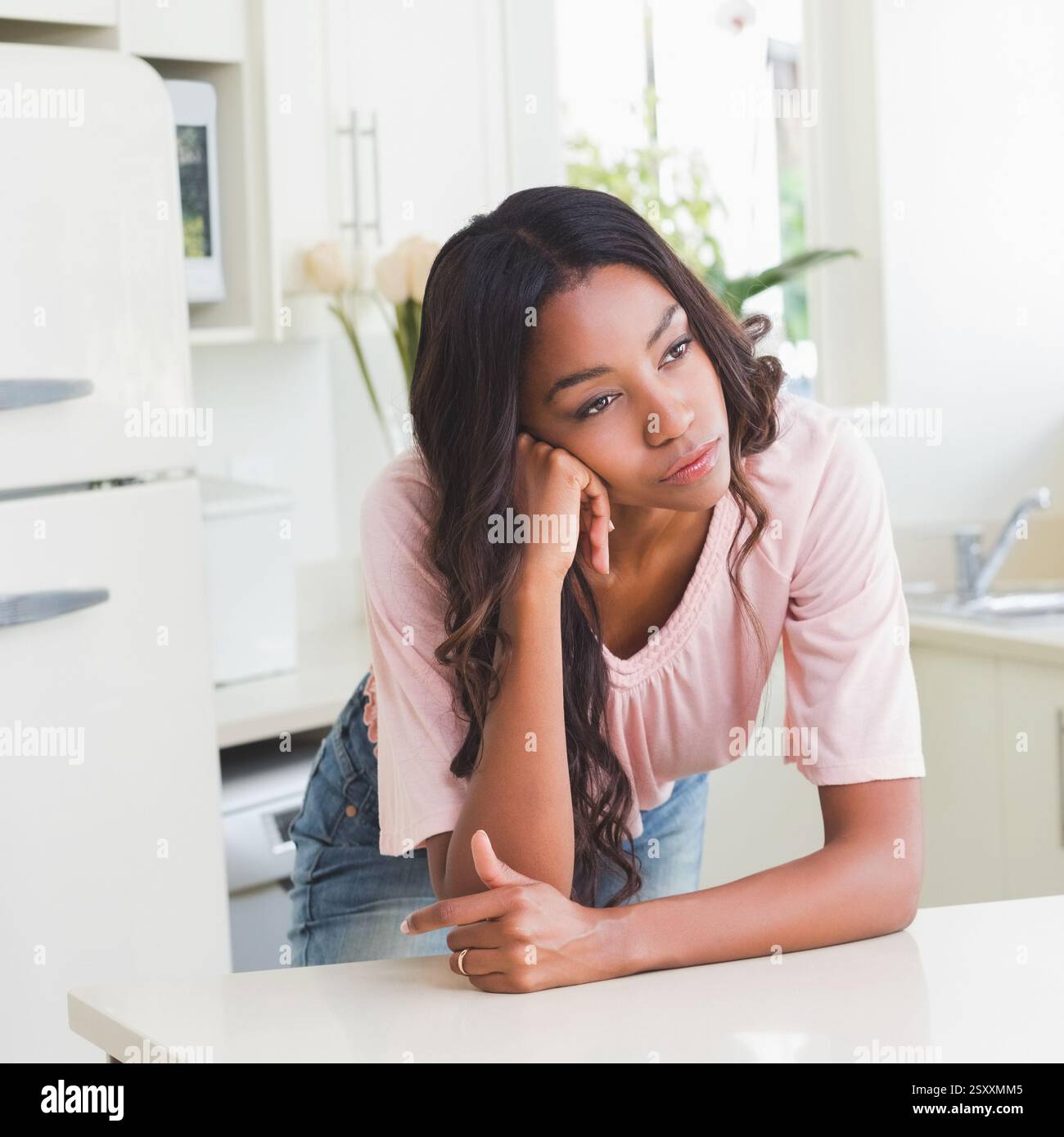 Femme appuyée sur le comptoir de la cuisine, rêvant dans une cuisine lumineuse et moderne Banque D'Images