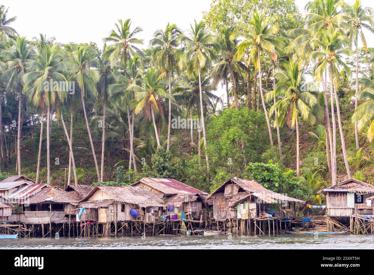 Bahay kubo, maisons Philippines traditionnelles sur pilotis construites au-dessus de la mer avec des matériaux légers et des cocotiers en arrière-plan à Surigao, Philippines Banque D'Images