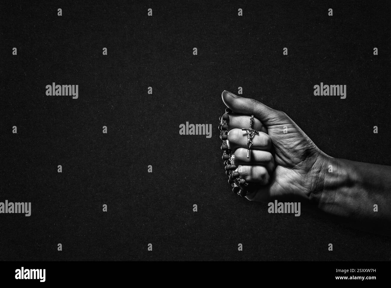 Main avec Rosaire et Croix en noir et blanc sur fond de papier texturé, espace de copie Banque D'Images
