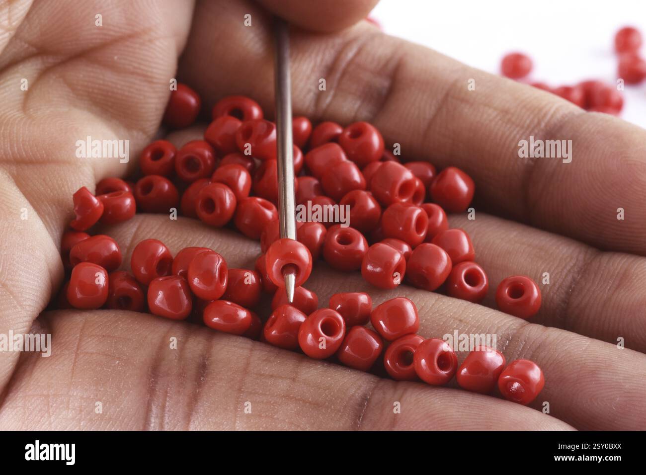 Gros plan photo de la main d'une femme clouant des perles sur une aiguille. Perles avec aiguille. macro, utilisé dans la finition des vêtements de mode. faire collier de perles, perles pour Banque D'Images
