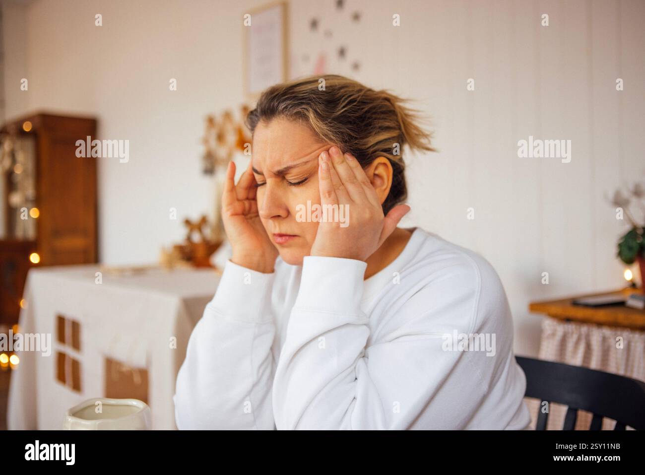 Luttant contre un mal de tête, elle s’assoit en silence, incarnant un moment de pensée profonde et de solitude. Son expression raconte une histoire de stress continu et c Banque D'Images