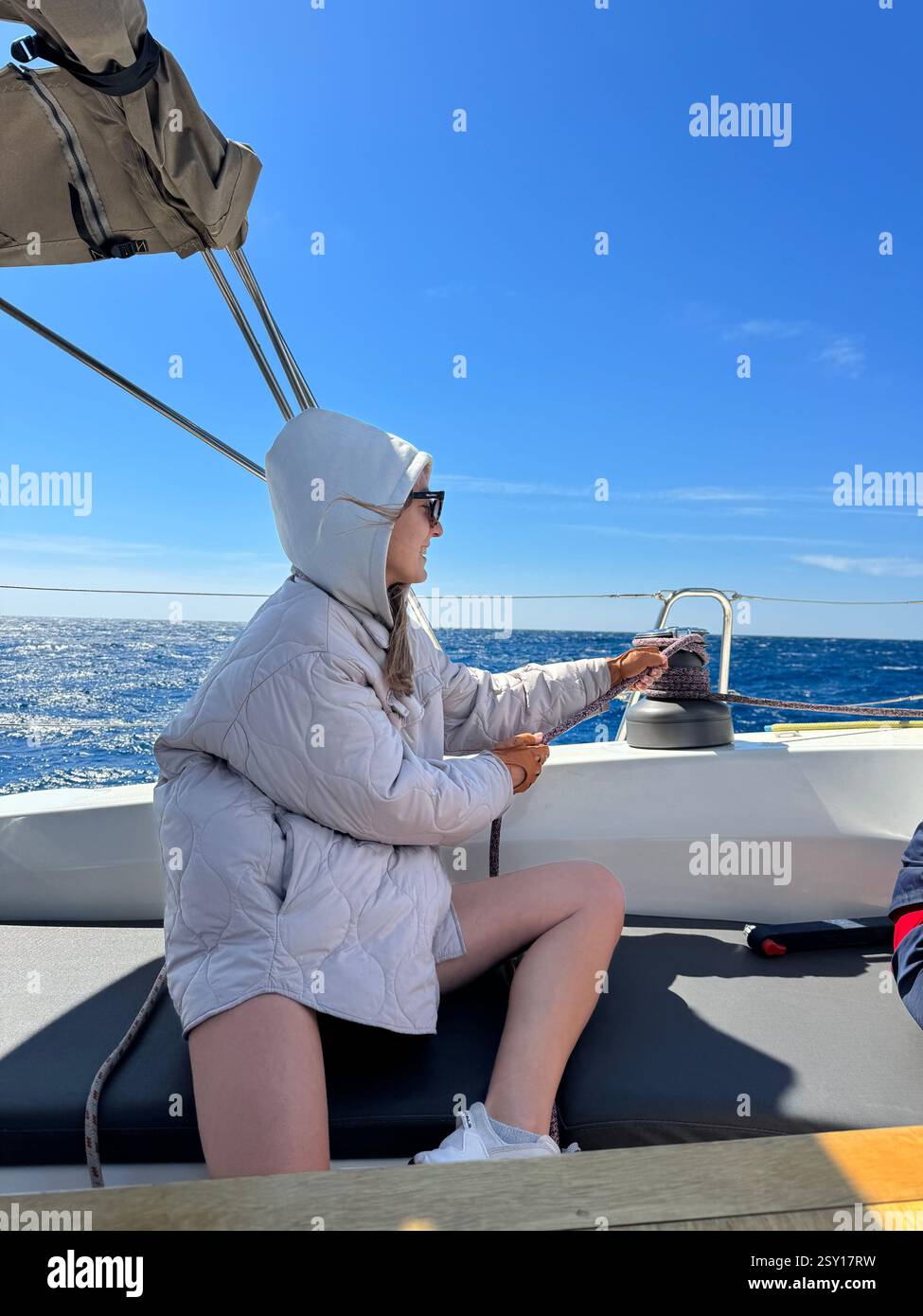 Jeune femme naviguant sur un bateau sous un ciel bleu clair tout en ajustant la voile Banque D'Images