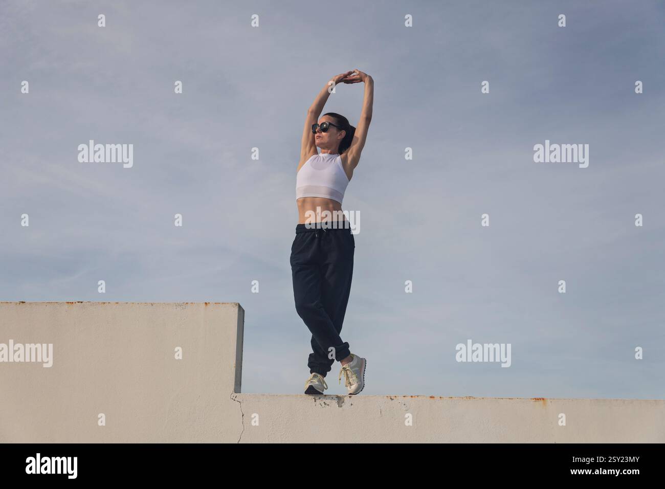 femme sportive debout sur un mur faisant un exercice d'étirement des bras, portant des bas de survêtement Banque D'Images femme sportive debout sur un mur faisant un exercice d'étirement des bras, portant des bas de survêtement Banque D'Images