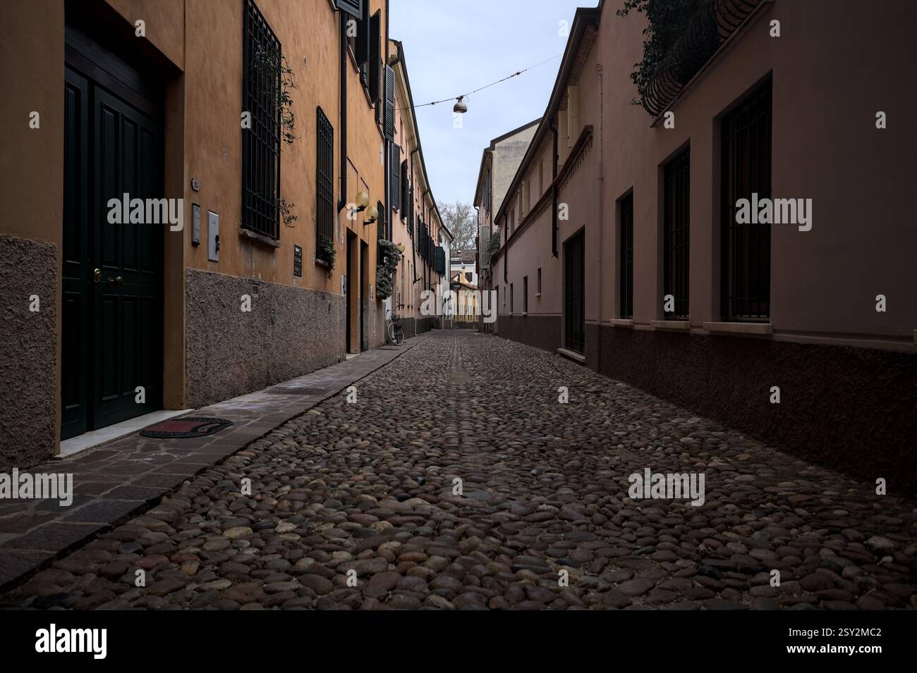 Étroite ruelle pavée avec des façades de bâtiments bas à l'ombre sur une journée nuageuse dans une ville italienne Banque D'Images Étroite ruelle pavée avec des façades de bâtiments bas à l'ombre sur une journée nuageuse dans une ville italienne Banque D'Images