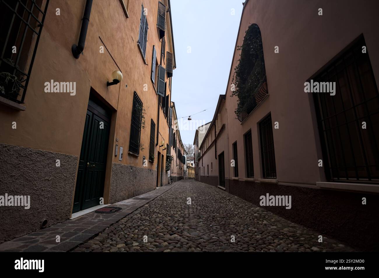 Étroite ruelle pavée avec des façades de bâtiments bas à l'ombre sur une journée nuageuse dans une ville italienne Banque D'Images Étroite ruelle pavée avec des façades de bâtiments bas à l'ombre sur une journée nuageuse dans une ville italienne Banque D'Images