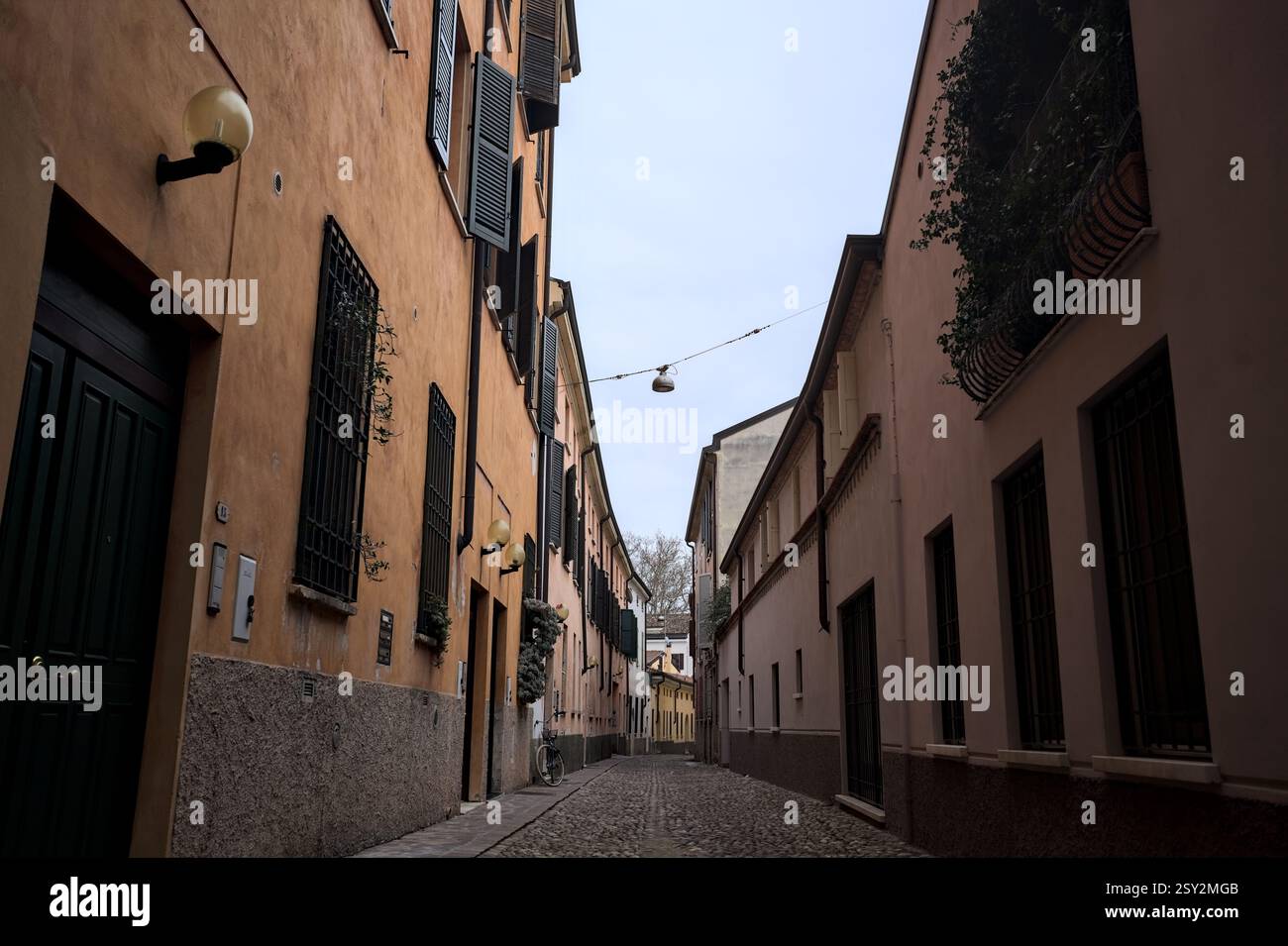 Étroite ruelle pavée avec des façades de bâtiments bas à l'ombre sur une journée nuageuse dans une ville italienne Banque D'Images Étroite ruelle pavée avec des façades de bâtiments bas à l'ombre sur une journée nuageuse dans une ville italienne Banque D'Images