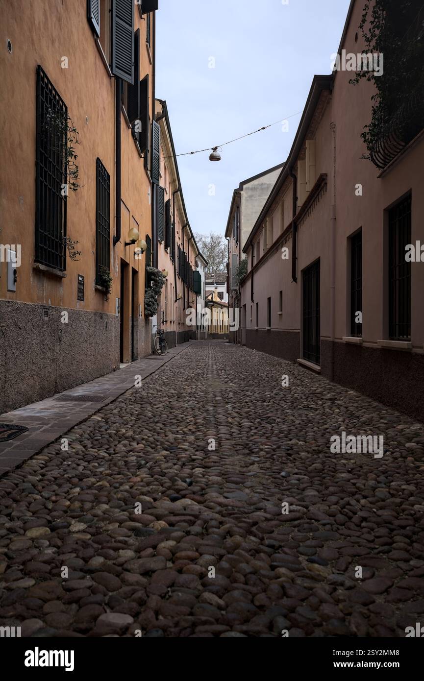Étroite ruelle pavée avec des façades de bâtiments bas à l'ombre sur une journée nuageuse dans une ville italienne Banque D'Images Étroite ruelle pavée avec des façades de bâtiments bas à l'ombre sur une journée nuageuse dans une ville italienne Banque D'Images