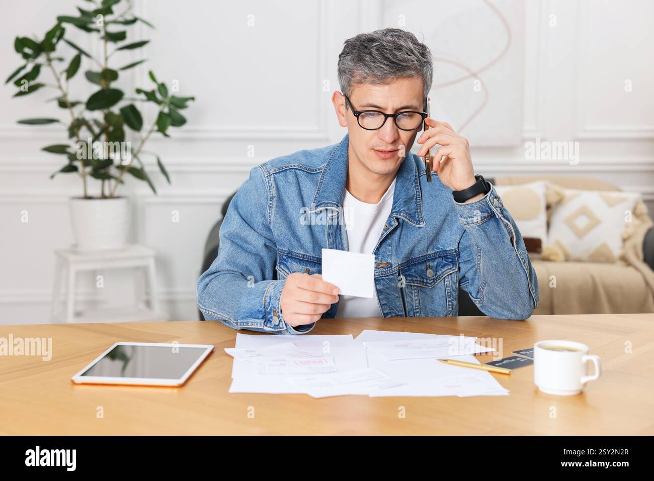 Payer des factures. Homme avec différentes factures parlant au téléphone à l'intérieur Banque D'Images