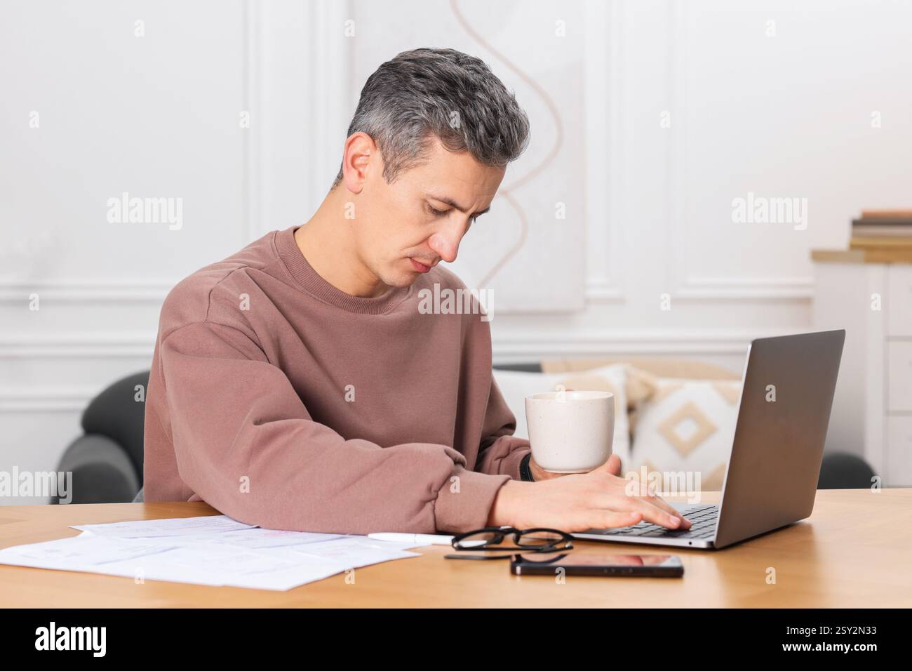 Homme payant des factures avec ordinateur portable à la table en bois à l'intérieur Banque D'Images